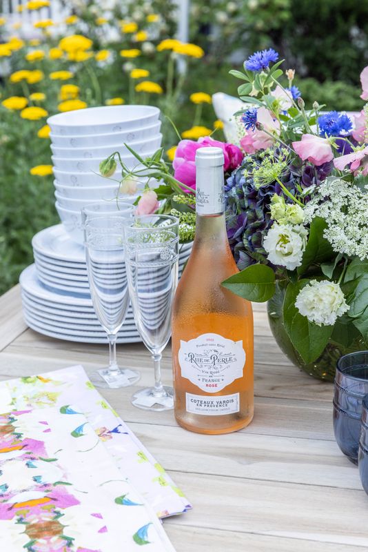 A summer table set with white dinnerware, flutes, rosé and garden flowers